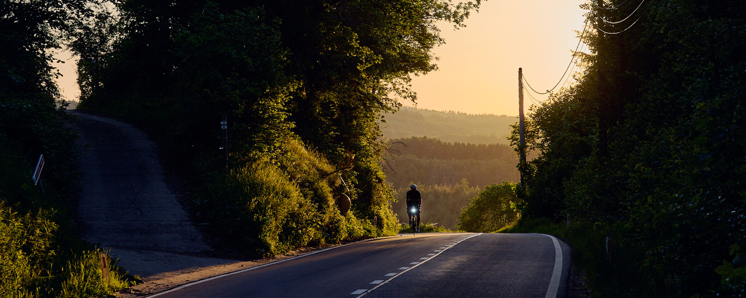 A rider on a quiet road through wooded hills at sunset